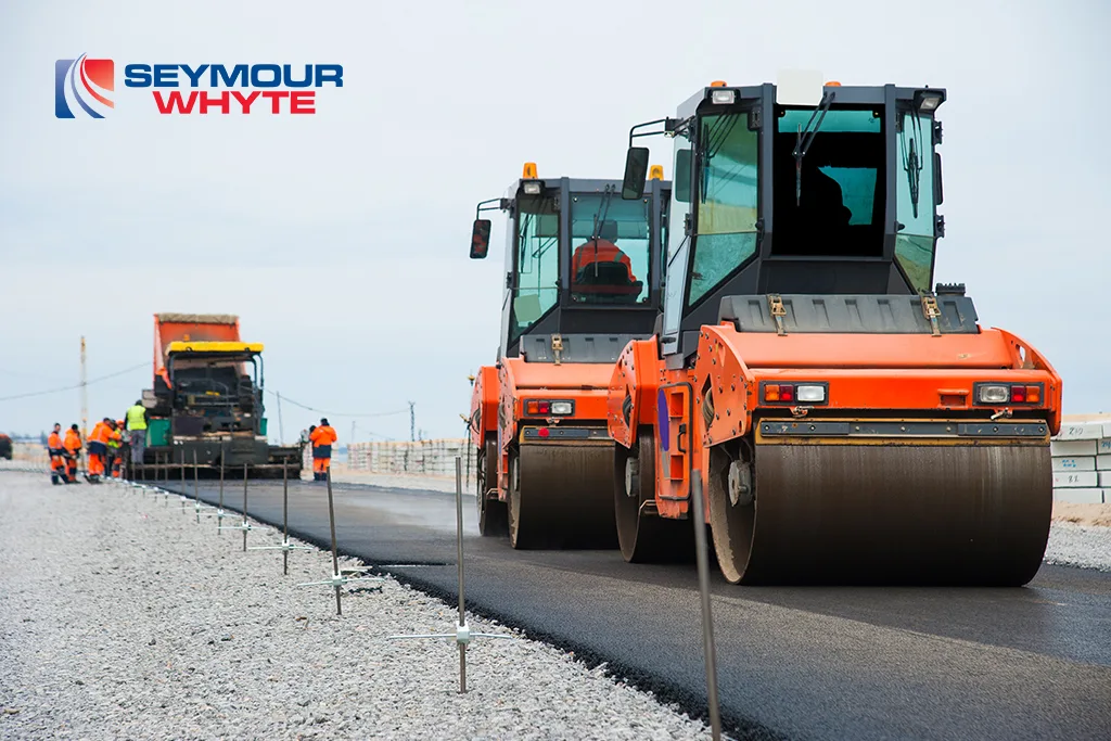 Road construction site with asphalt rollers and a paving train