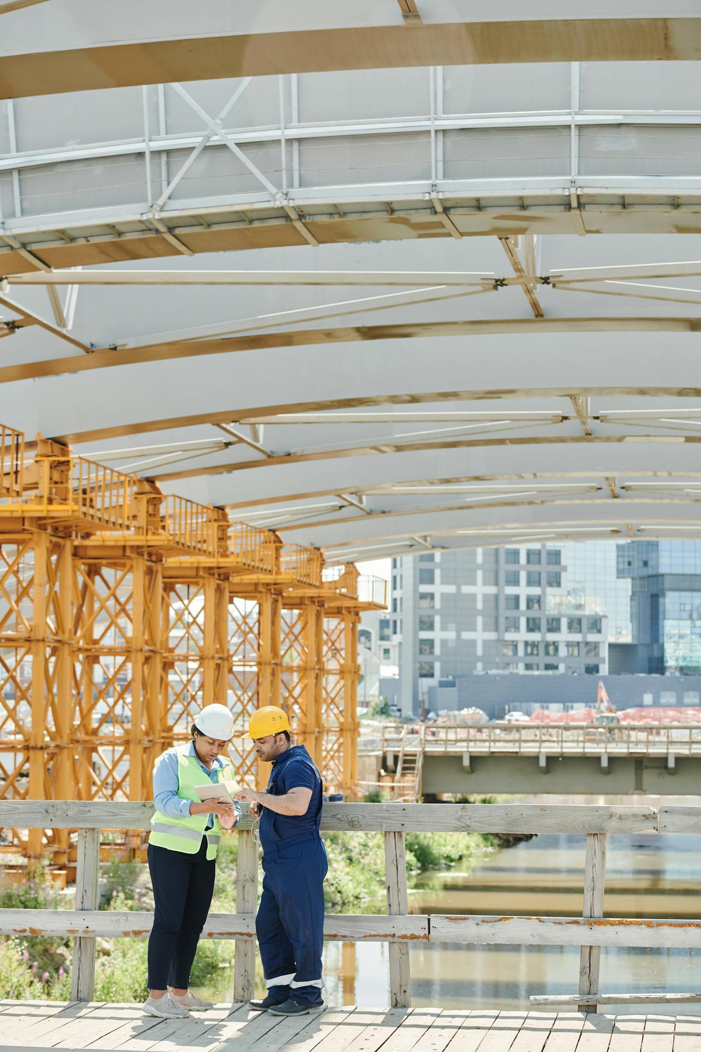 ScheduleReader 19 Two engineers discussing plans at an outdoor construction site under a bridge.
